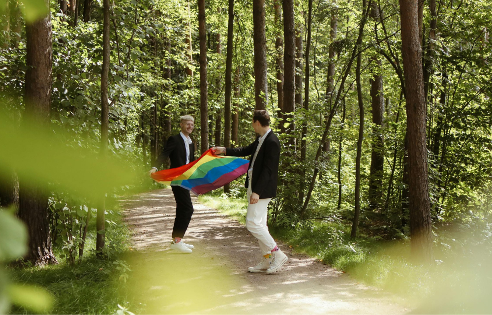 A male couple holding a rainbow flag in the woods