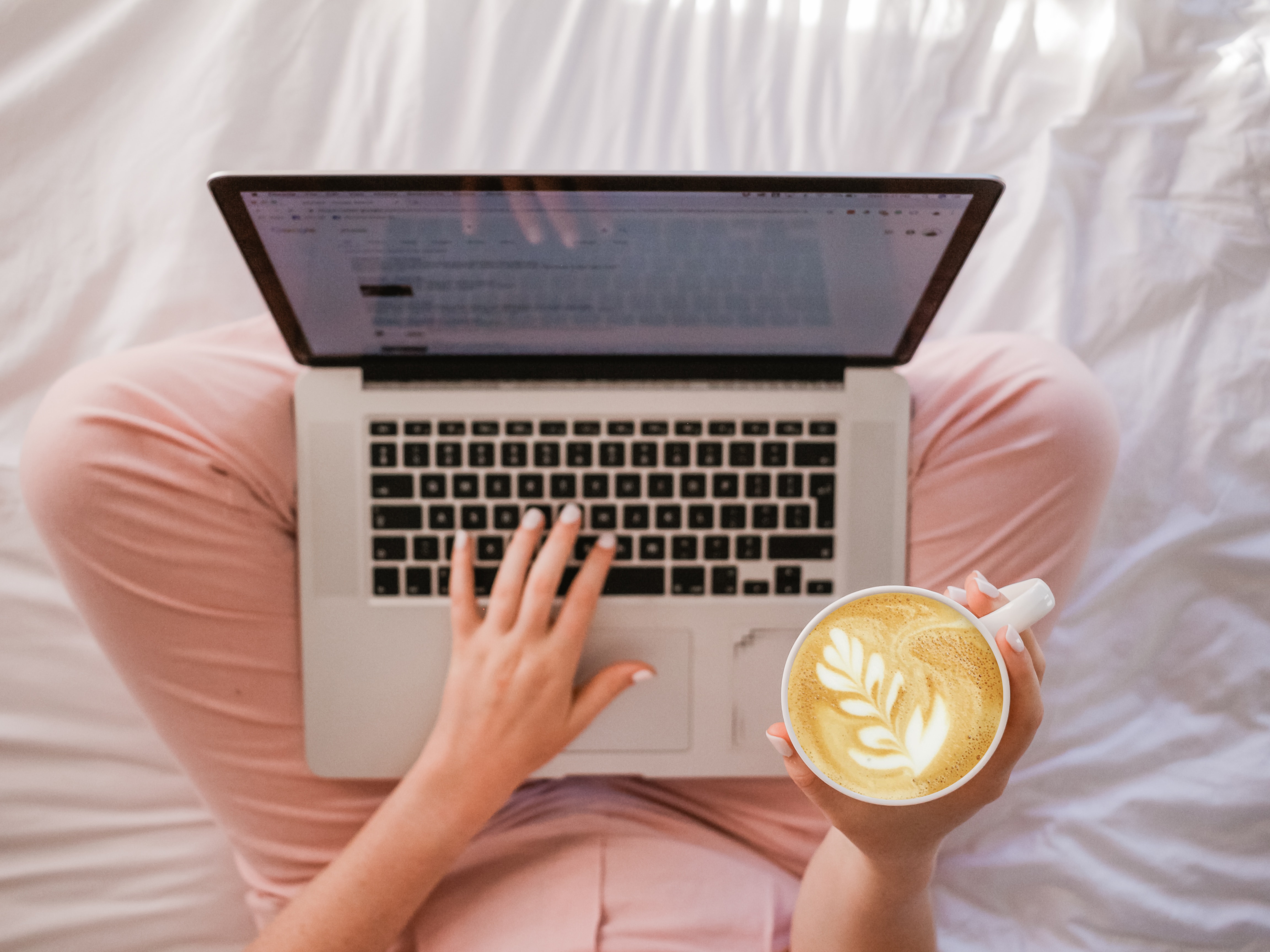laptop perched on woman's lap with pink pants and cup of coffee