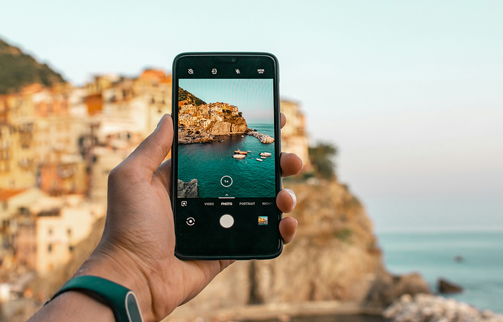 hand holding a phone while taking a photo of the beach cliff view in front