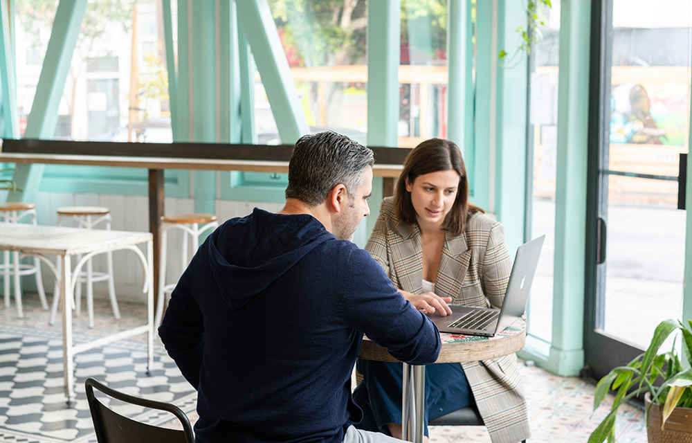 Two people facing a laptop and having a meeting on a coffee table inside a café.