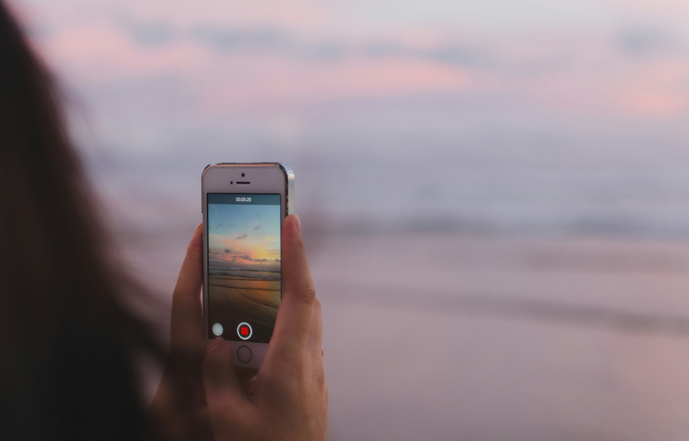 person holding a camera and taking video of a pink-ish sunset on a beach