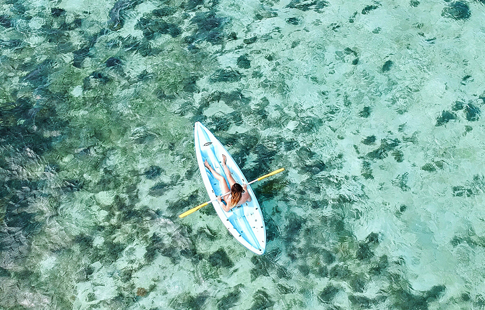 A woman sitting above a paddle board floating above gentle sea waves of a crystal clear beach