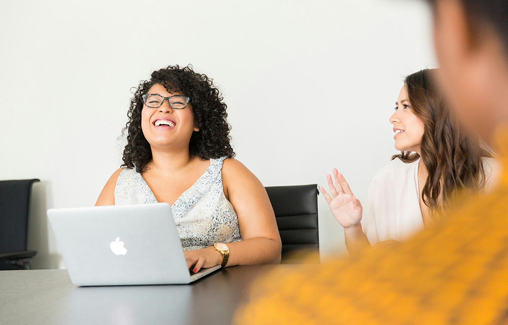 A woman with her laptop happily engaging with her coworkers while having a team discussion