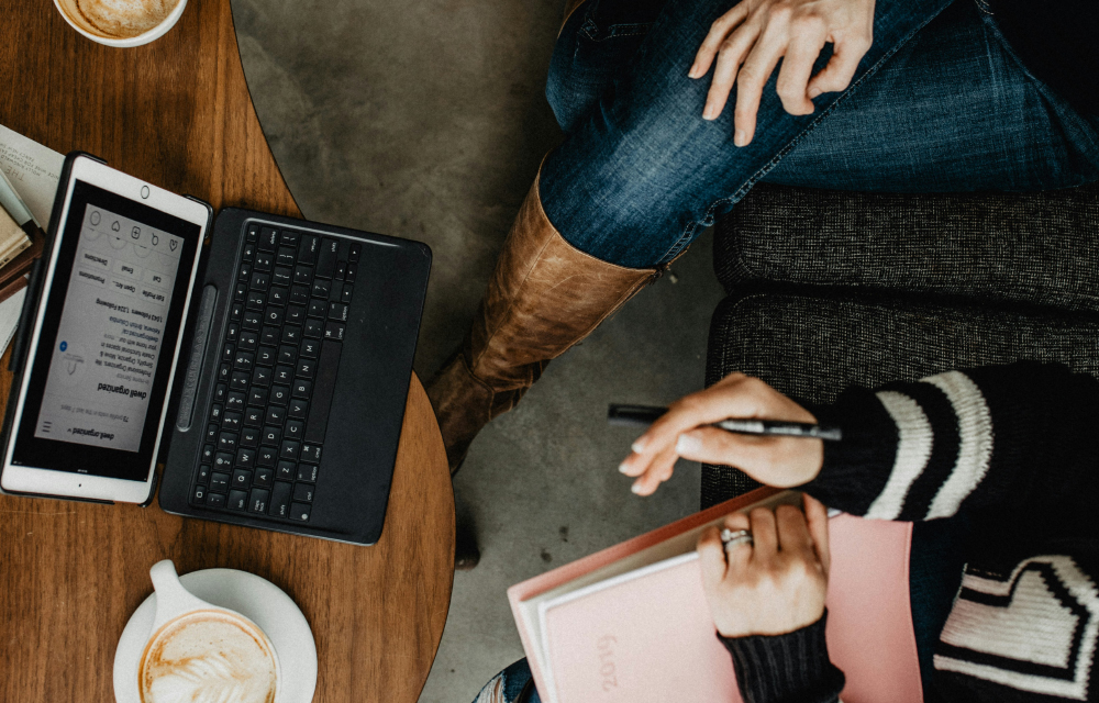 Two people working on a project, on a desk with a laptop, coffee, and notes.