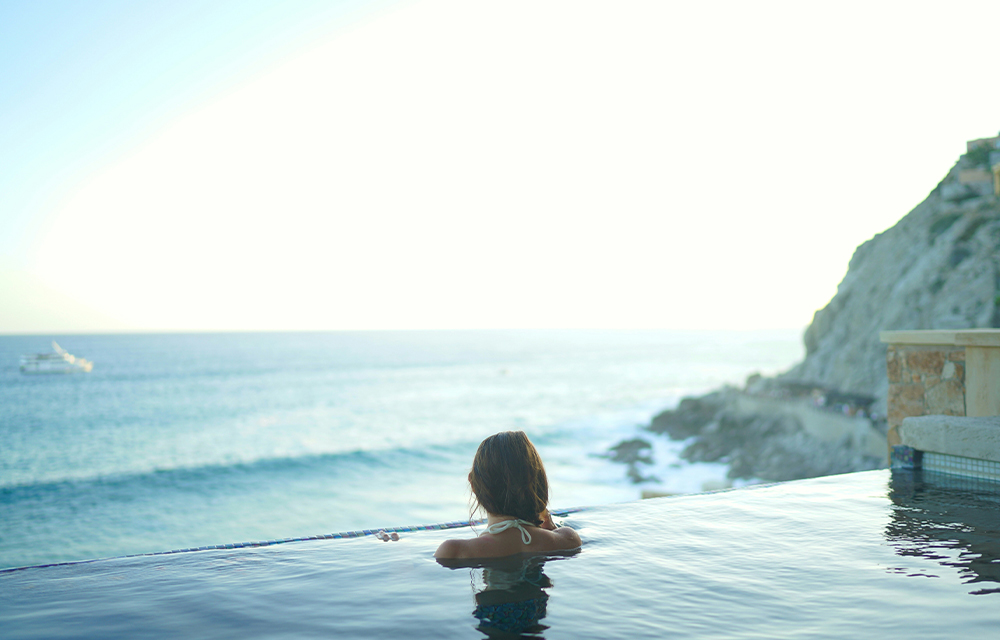 An influencer looking over a beach view in front of an infinity pool