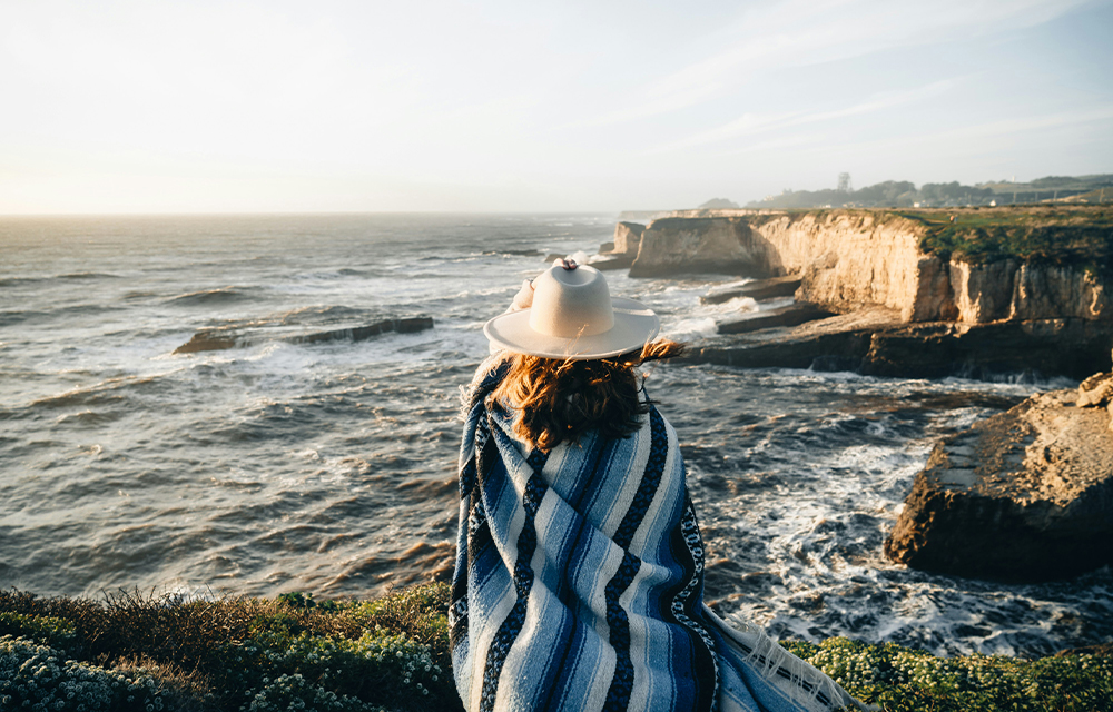 A woman overlooking the ocean and rocky shoreline at sunset.